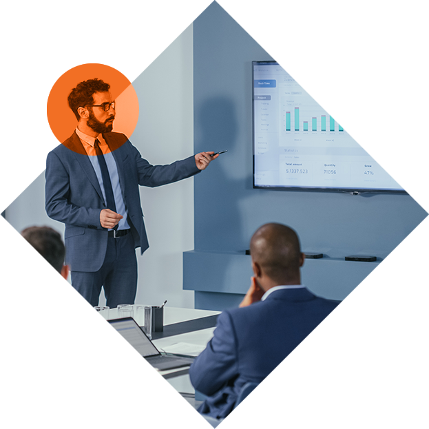 Man in suit presenting data to colleagues in a meeting in office conference room.